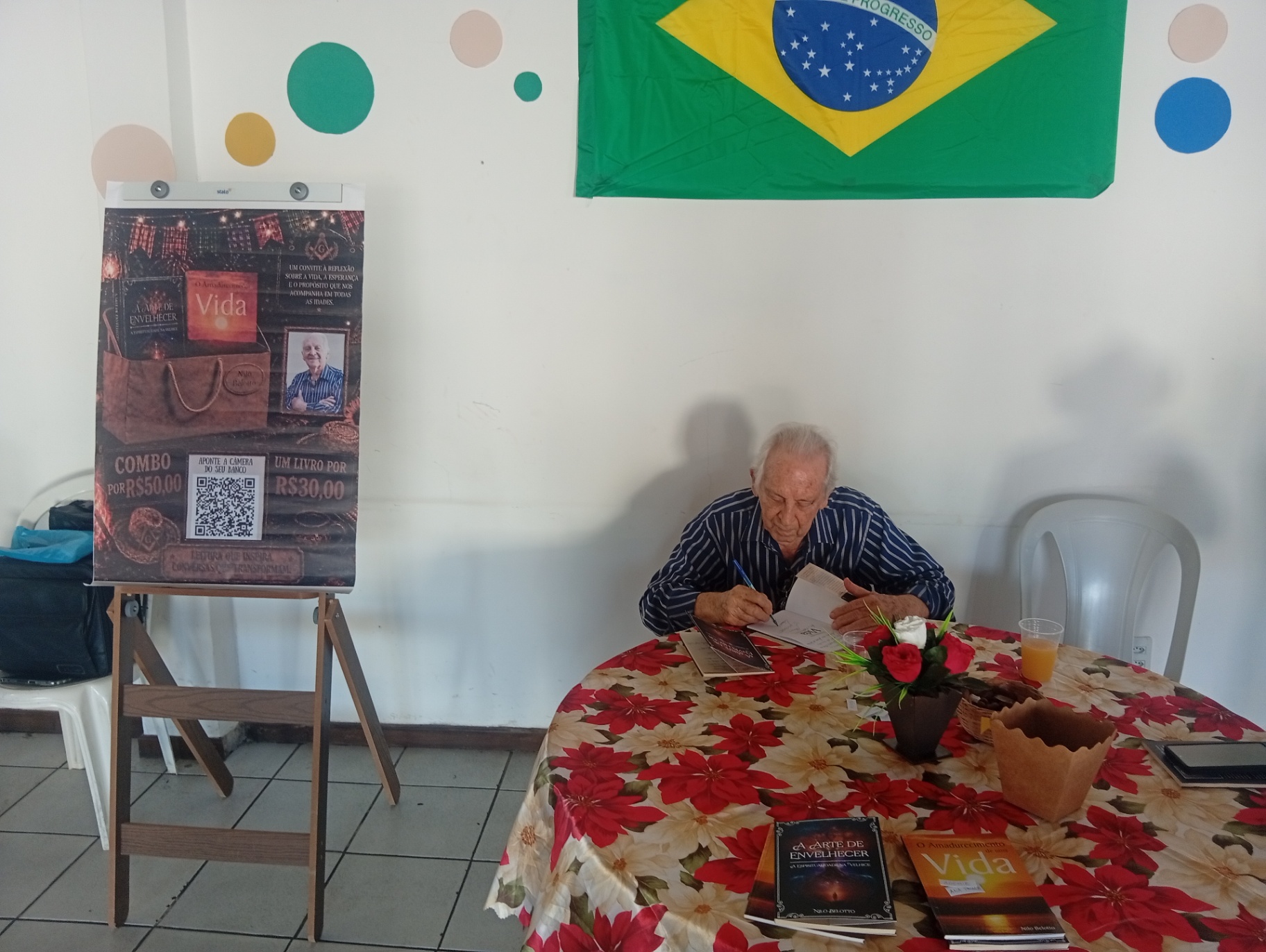 O autor concentrado, autografando livros sobre a mesa do evento.